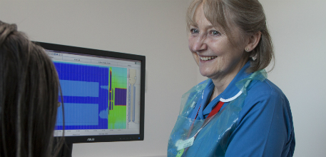 A nurse standing by a screen, smiling at a patient.