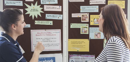 A member of staff and a pregnant woman looking at the information board.