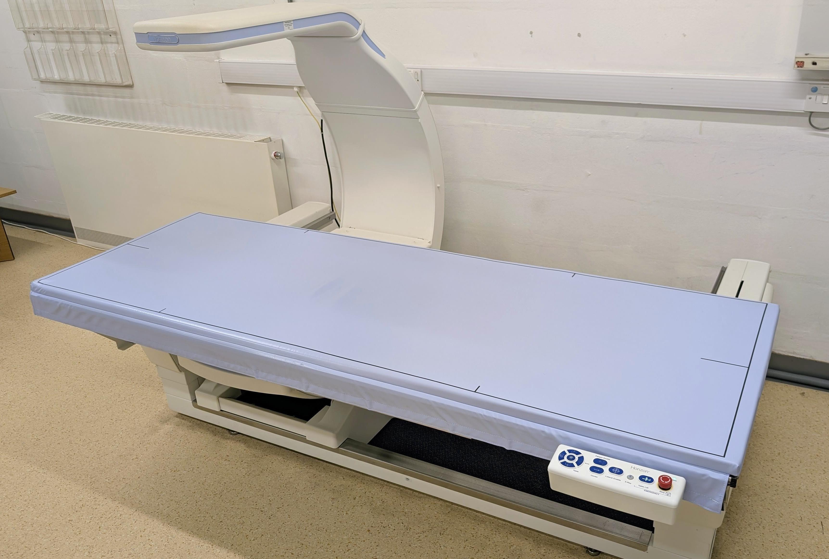 A DEXA scanner, showing a flat blue bed with a scanner arm over the top.