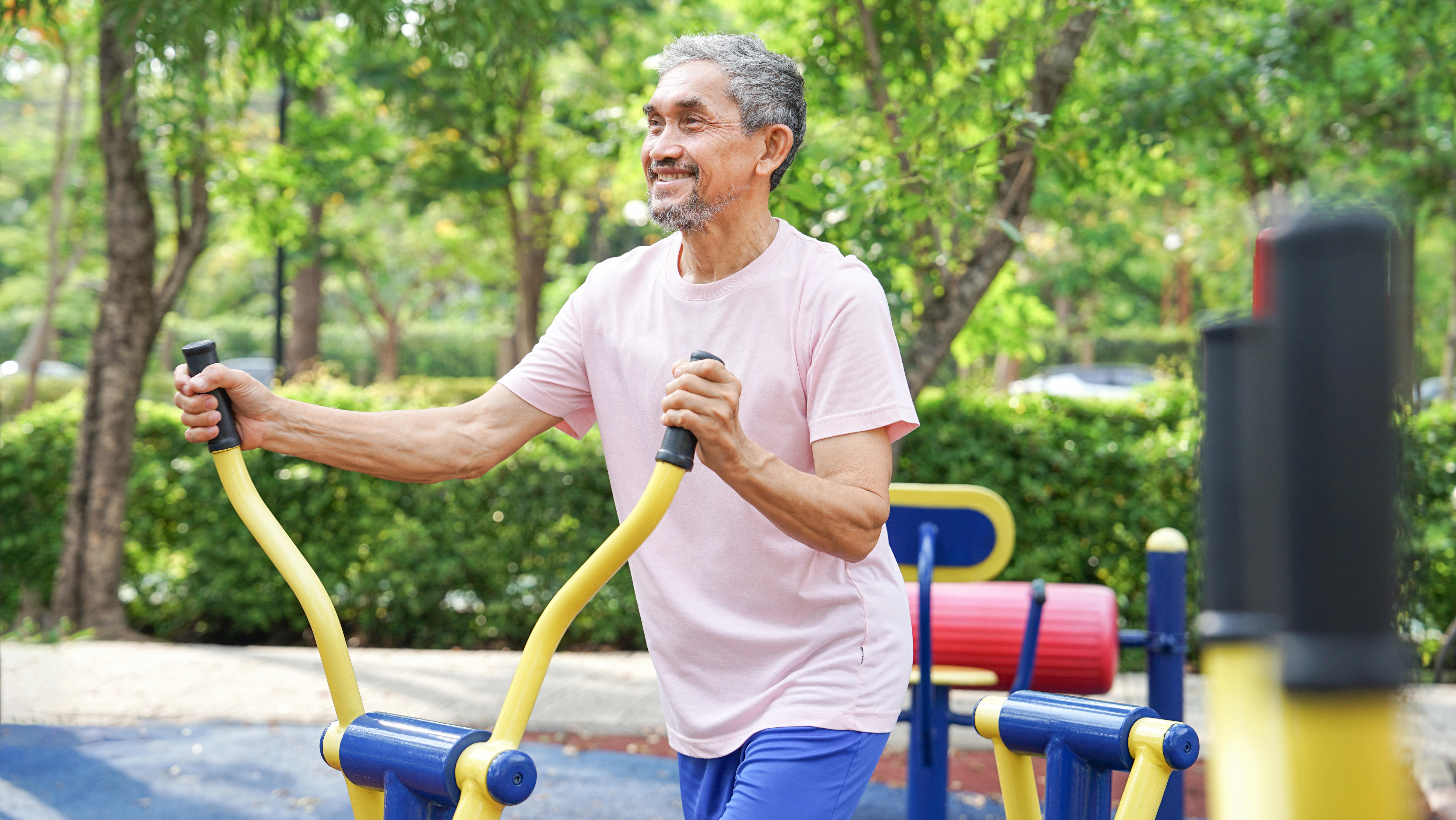 Man smiling while he uses outdoor exercise equipment.
