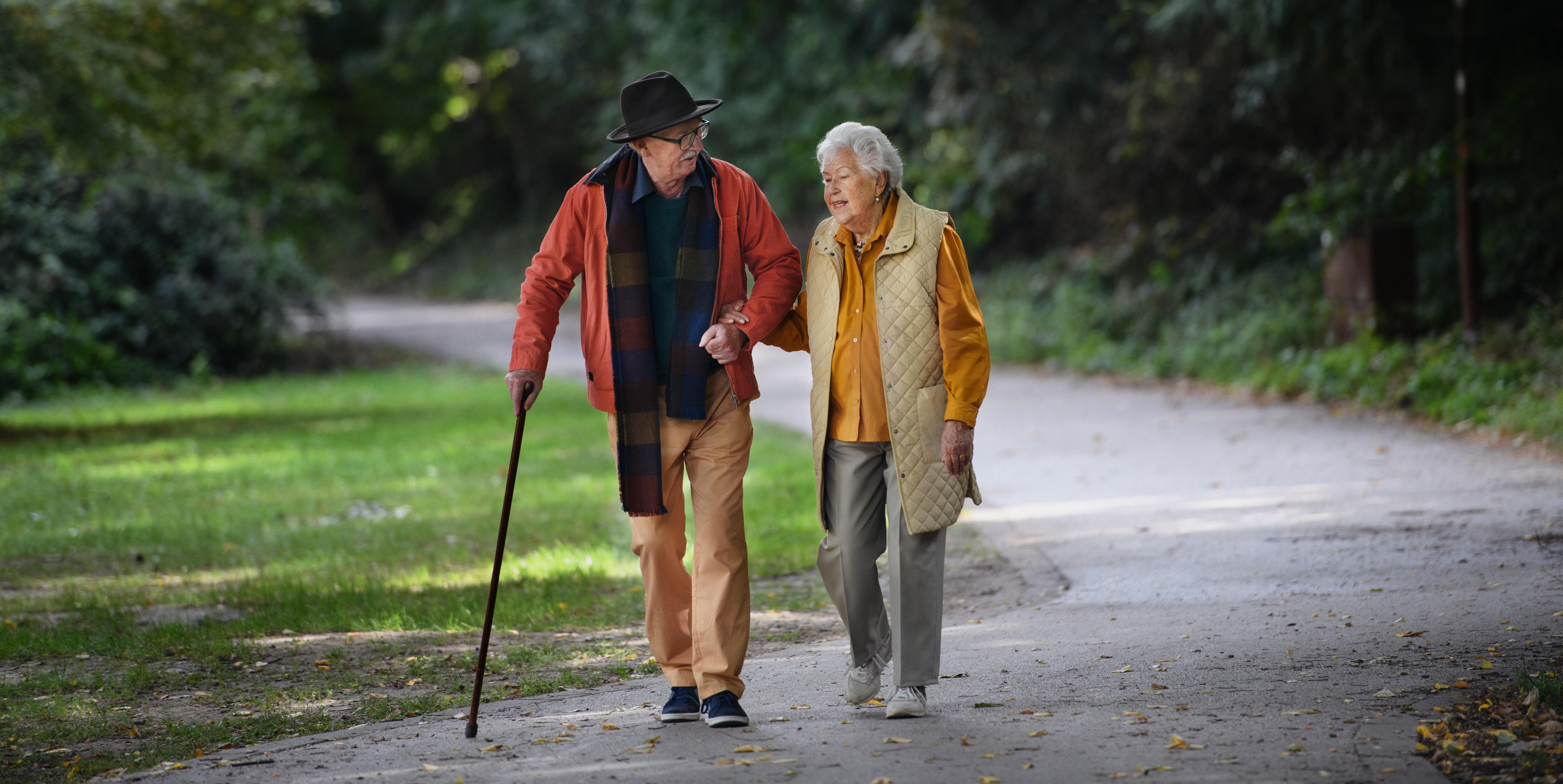 Two people walking together, one with a walking stick.